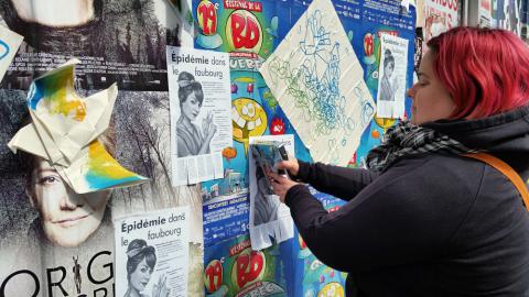 Photo : Marie-Ève du ComPop installe une affiche sur un ancien mur extérieur couvert d'affiches.
